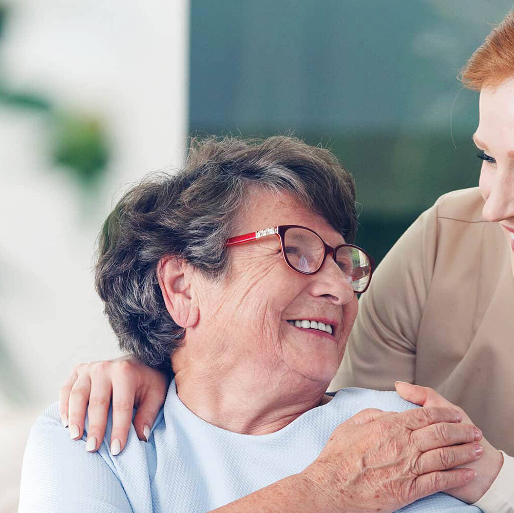 A close-up of a female caregiver and an older woman holding hands and looking at each other. Traditions at Hunter Station in Sellersburg, IN