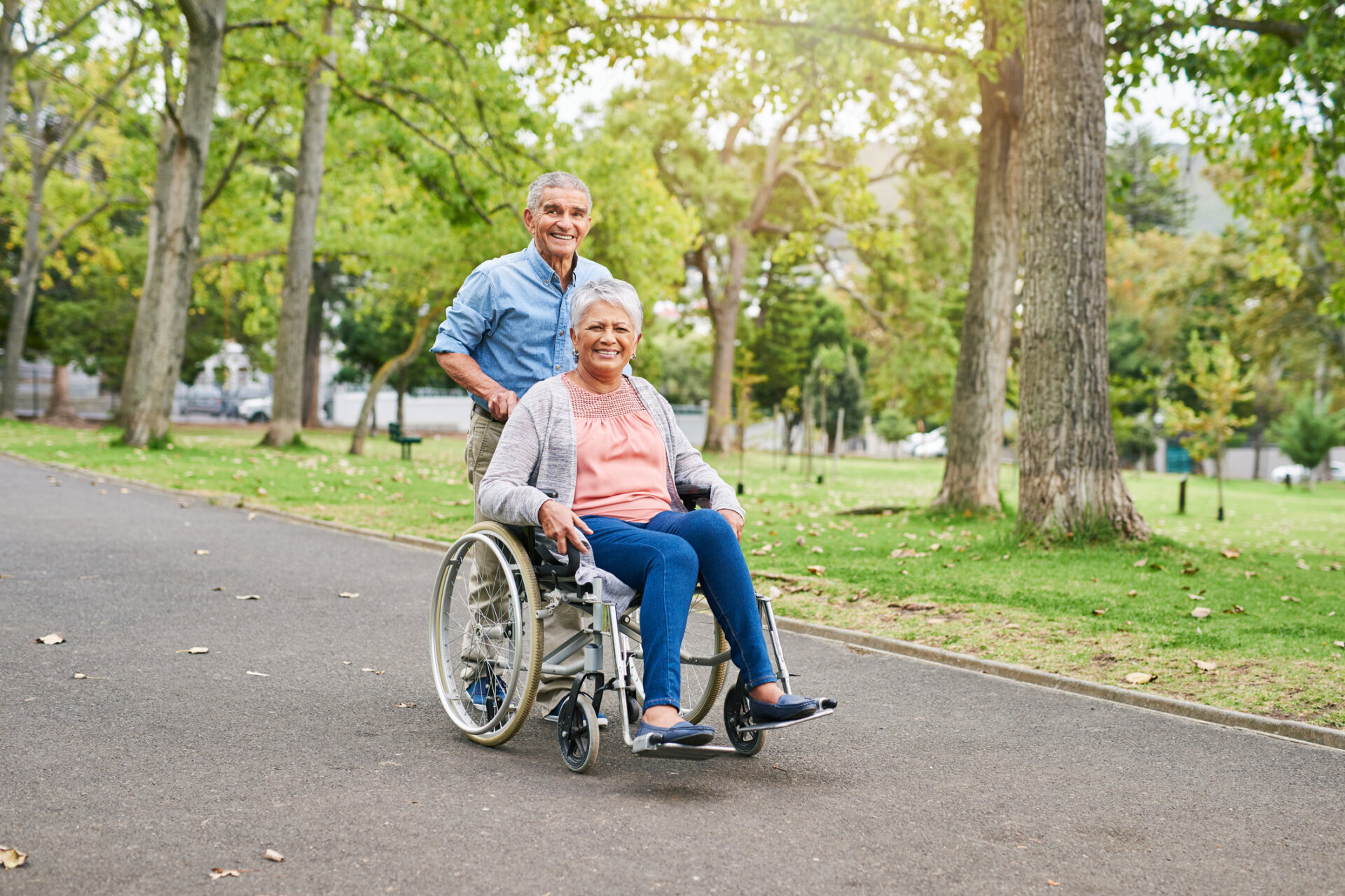 Senior man pushing his senior wife in a wheelchair outside of the Traditions at Hunter Station senior community