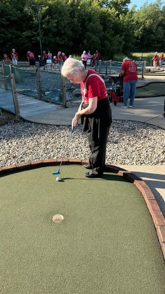 Resident enjoying a round of mini golf during a community outing from Traditions at Hunter Station
